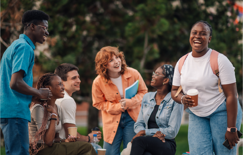 group of college students gathered sitting outside in an group smiling and laughing together