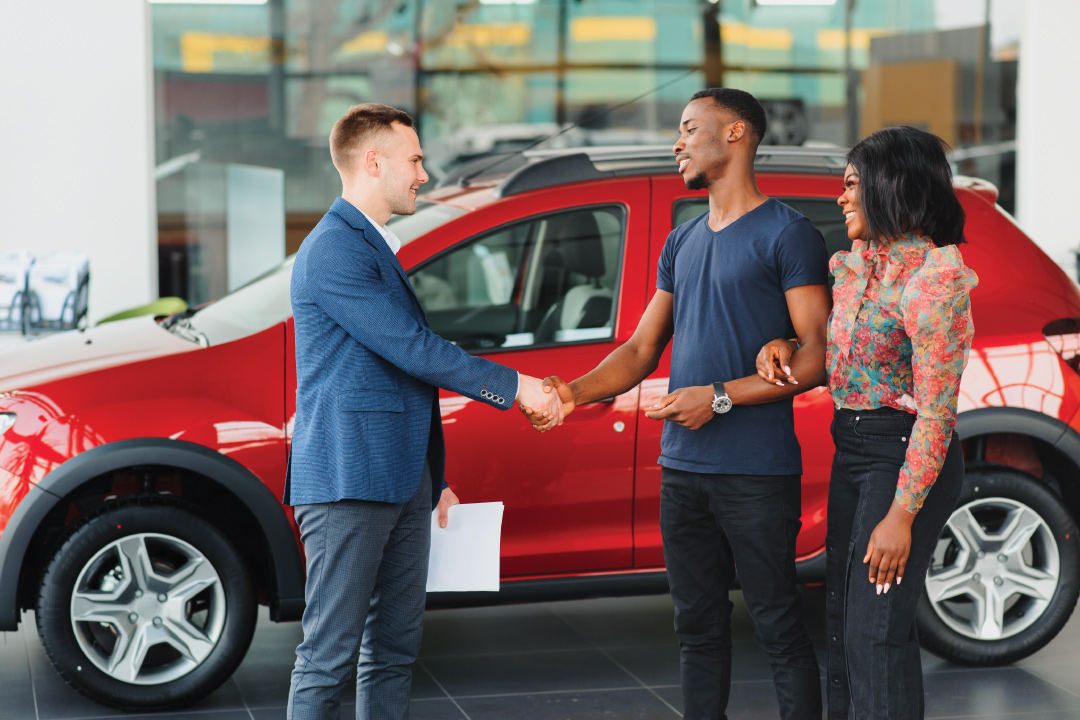 young African American couple shaking hands with car salesman at dealership