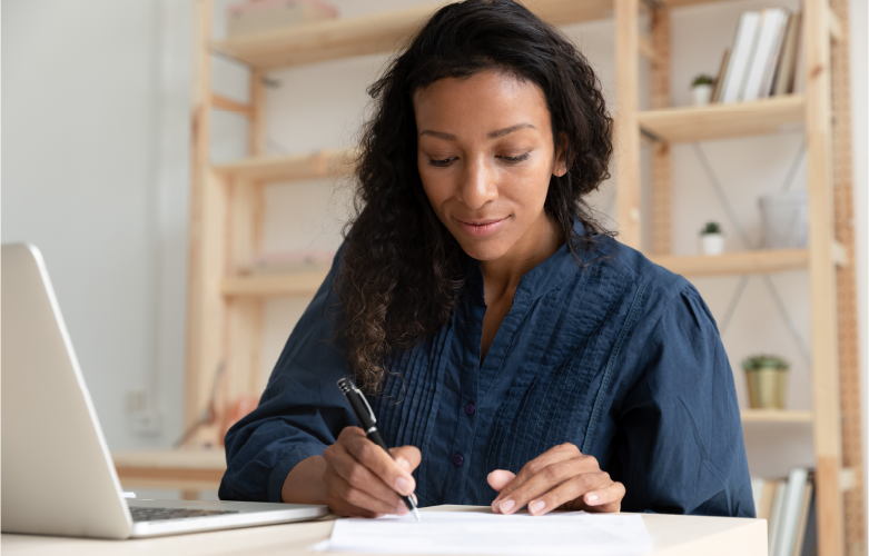 young adult woman sitting at counter with laptop writing out check