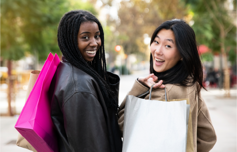 two college friends smiling as they look back for a photo while holding shopping bags