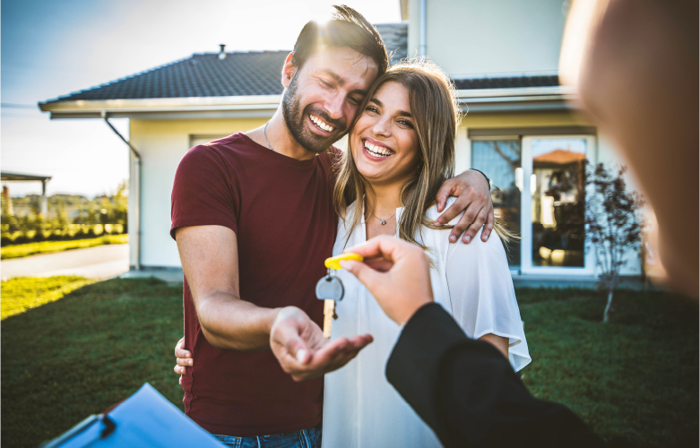 young adult couple smiling brightly as they are presented keys to their new home