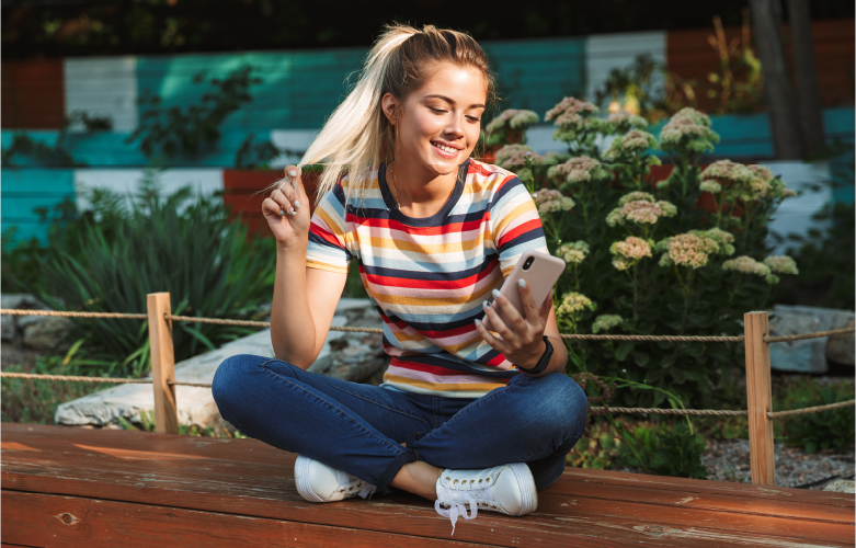 female college student sitting outside on bench using smartphone