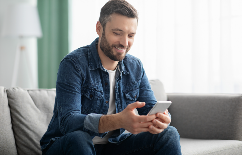 adult male wearing denim shirt smiling as he's checking his banking account with his phone