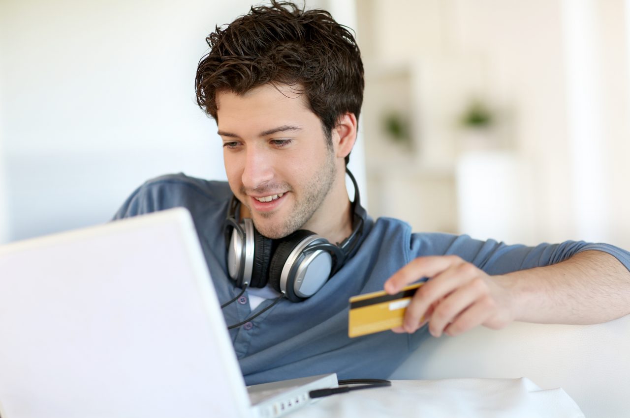 guy looking a laptop with credit card in his hand with headphones around his neck