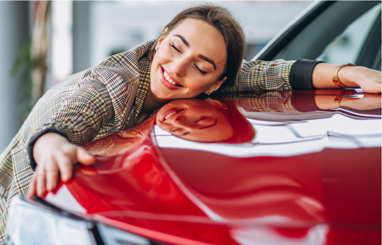 young female adult smiling brightly and hugging her new car on the sales showroom