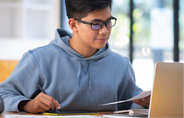 asian American young adult wearing blue hoodie and smiling while working on laptop