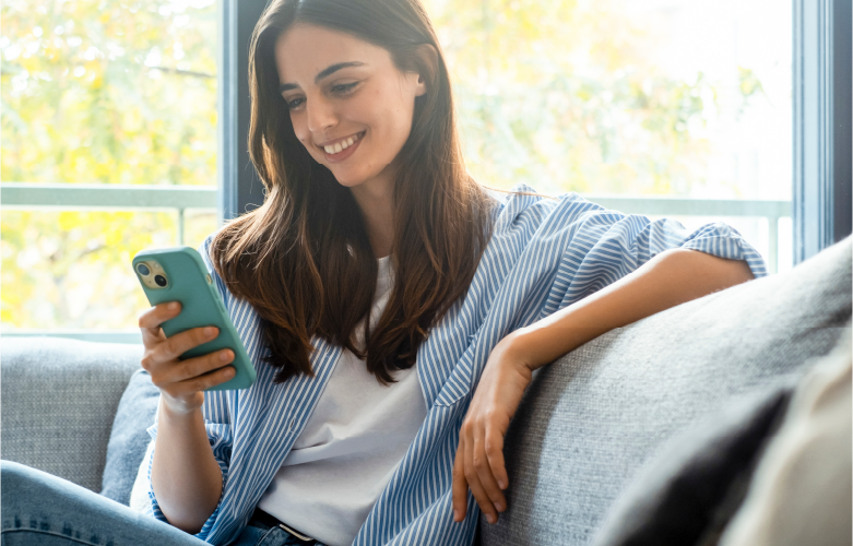 female college student sitting cozily on a couch using smartphone