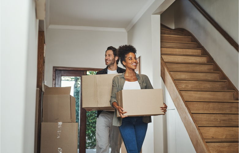 adult couple carrying boxes and smiling as they move into their new home