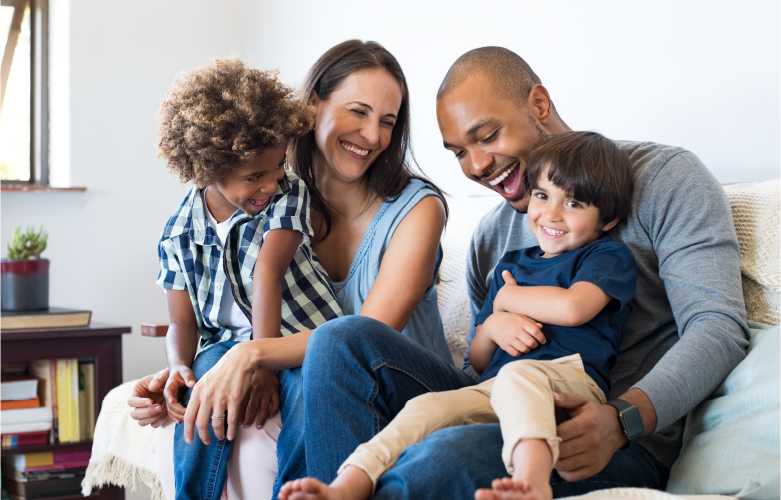 family sitting together closely on couch all smiling warmly
