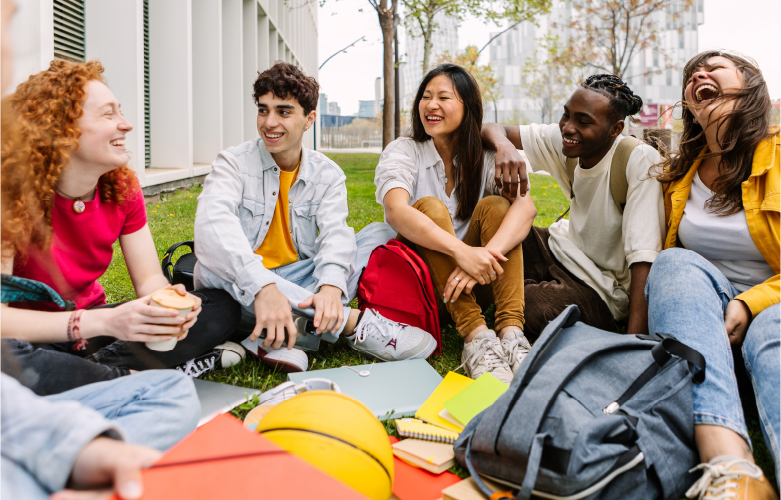group of college students gathered sitting outside in an group smiling and laughing together