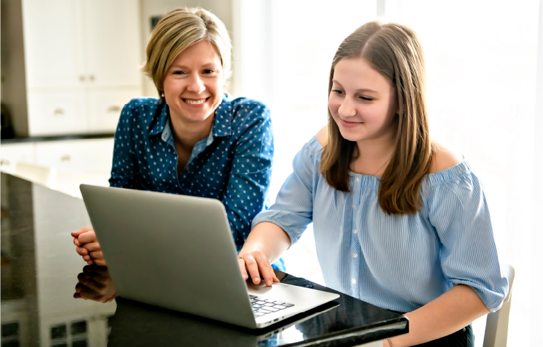 mother sitting with teenage daughter at laptop computer teaching her about her bank account