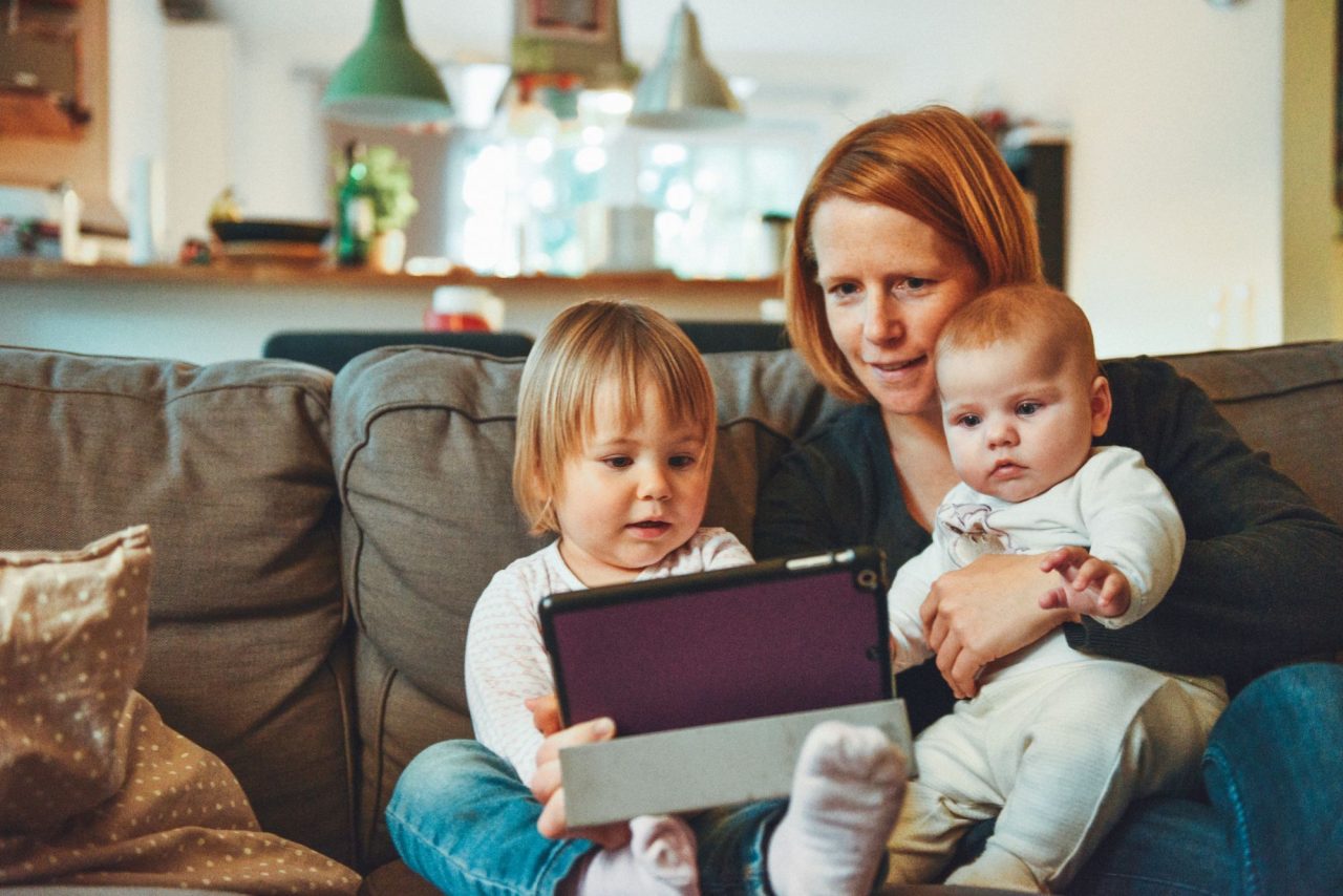 mother with two young children on couch holding tablet for online banking
